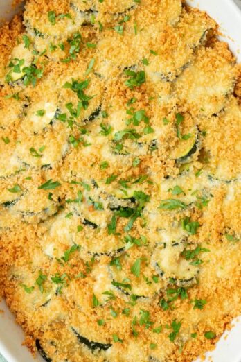 Zucchini casserole baked in an oval dish with a golden brown breadcrumb topping, garnished with fresh chopped parsley.