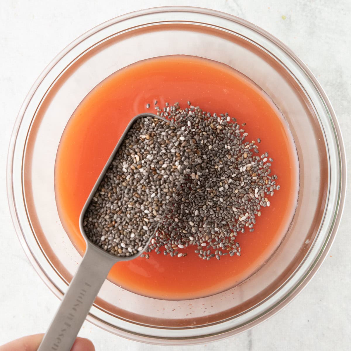 A measuring spoon full of chia seeds being trickled on top of juice in the jar.