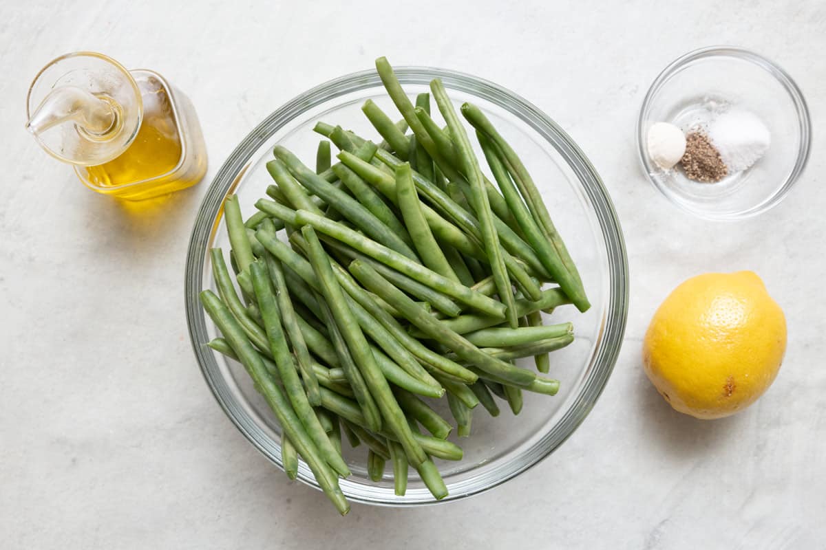 Ingredients for recipe: oil, bowl of fresh green beans, seasonings, and lemon.