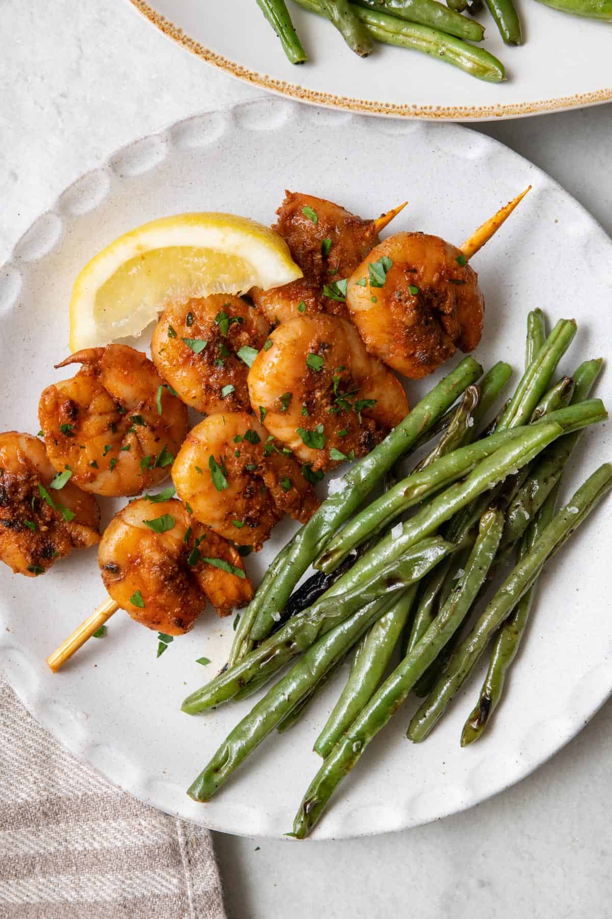 Grilled green beans on a plate with seasoned shrimp skewers.