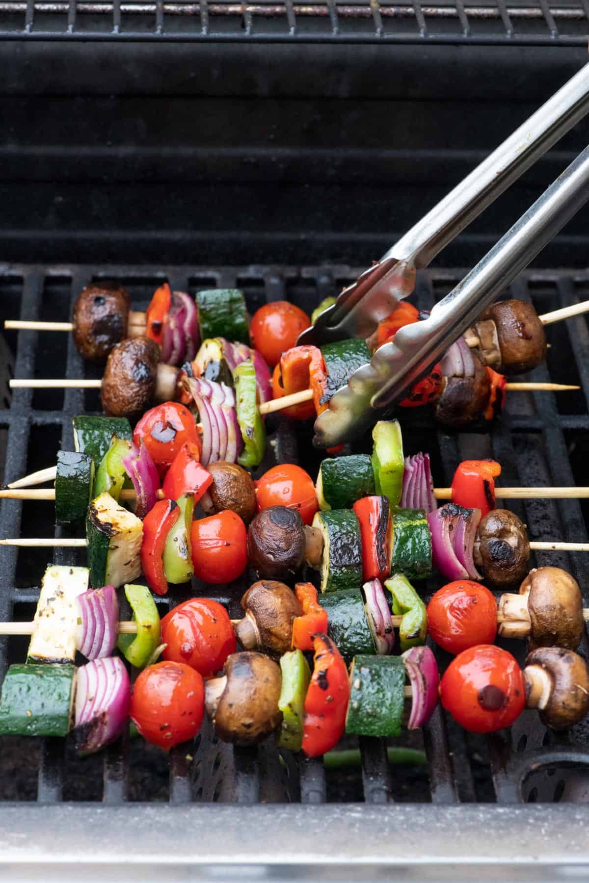 Tongs lifting up a veggie skewer to flip over on the grill with more.