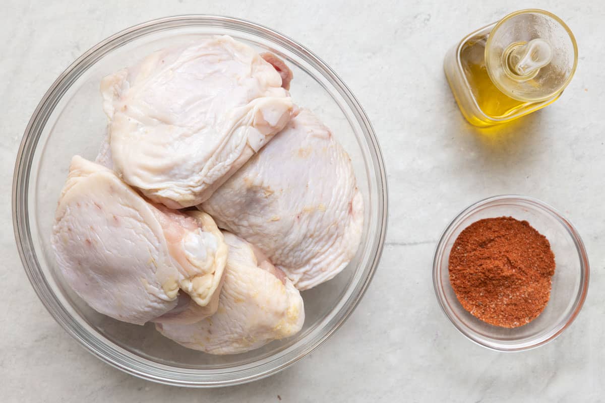 Ingredients for recipe: raw chicken thighs in a bowl, oil, and bbq seasoning.