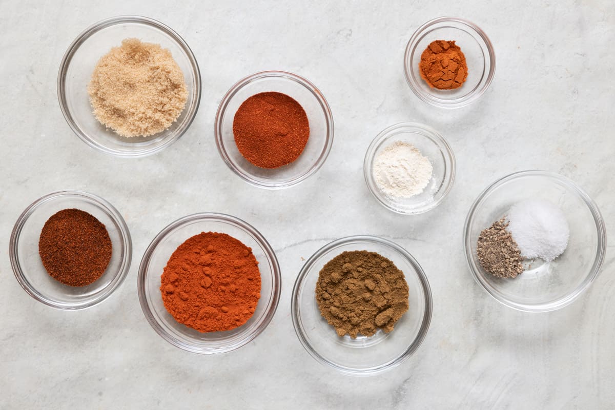 Spices for seasoning blend in individual bowls: smoked paprika, brown sugar, paprika, chili powder, cumin, garlic powder, salt, pepper, and cayenne.