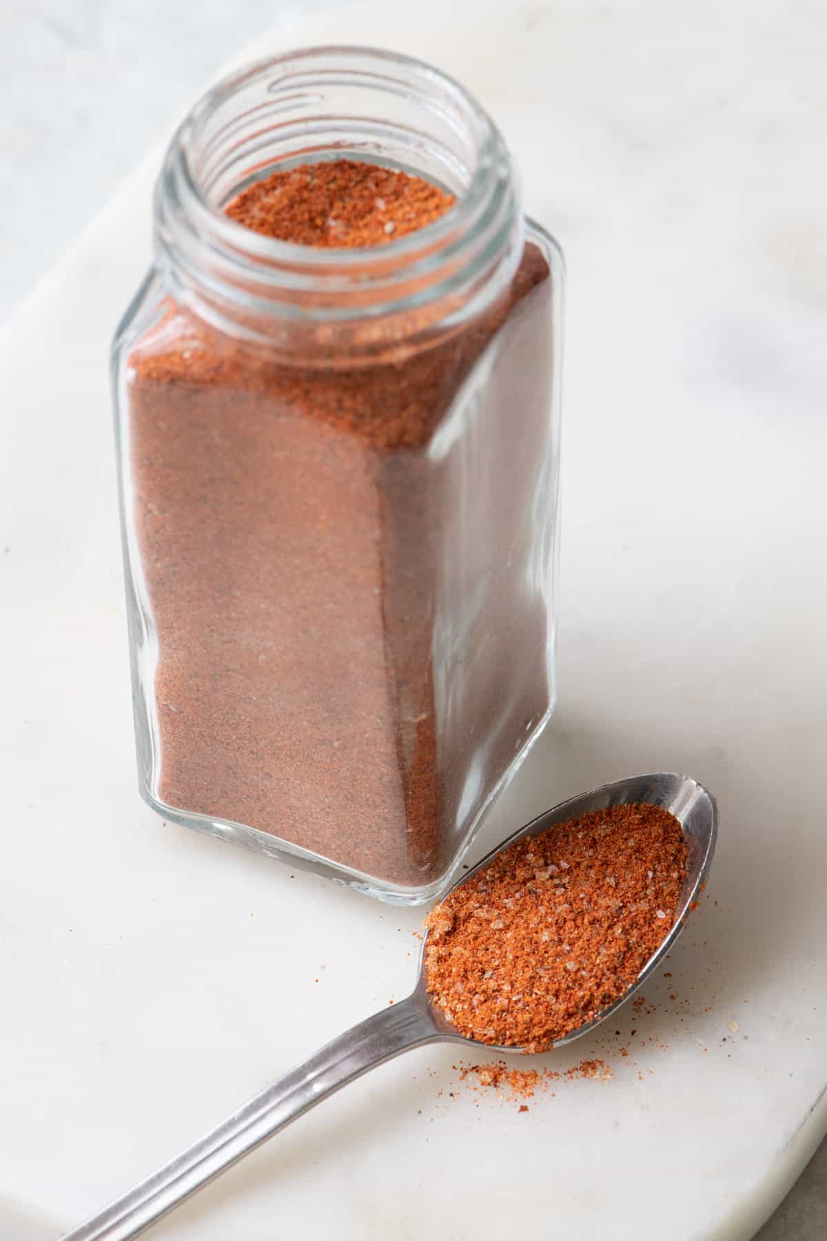 Small spice jar of homemade bbq seasoning blend with a spoon overfilling with some.