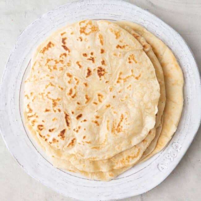 A stack of flour tortillas on a plate.