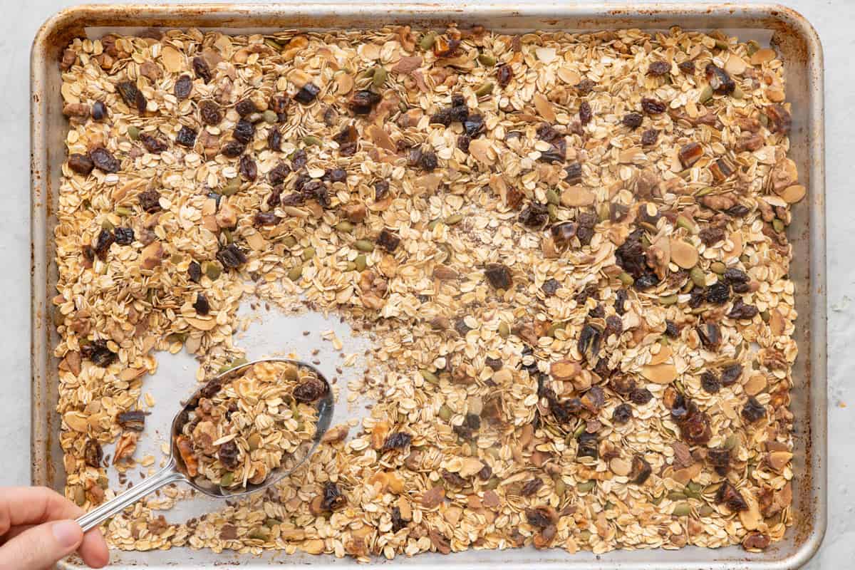 Toasted muesli on a baking sheet with a spoon scooping some up.