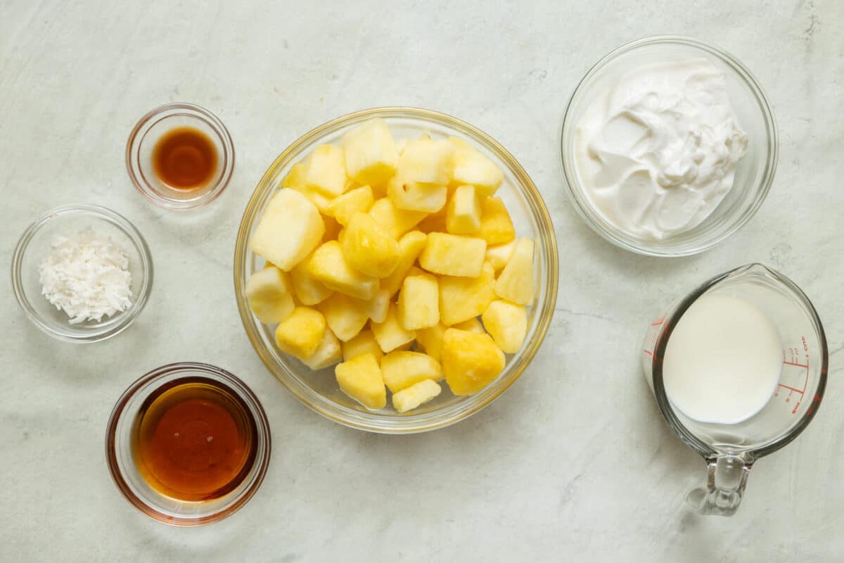 Ingredients for recipe: vanilla, maple syrup, frozen pineapple, coconut, yogurt, and milk.