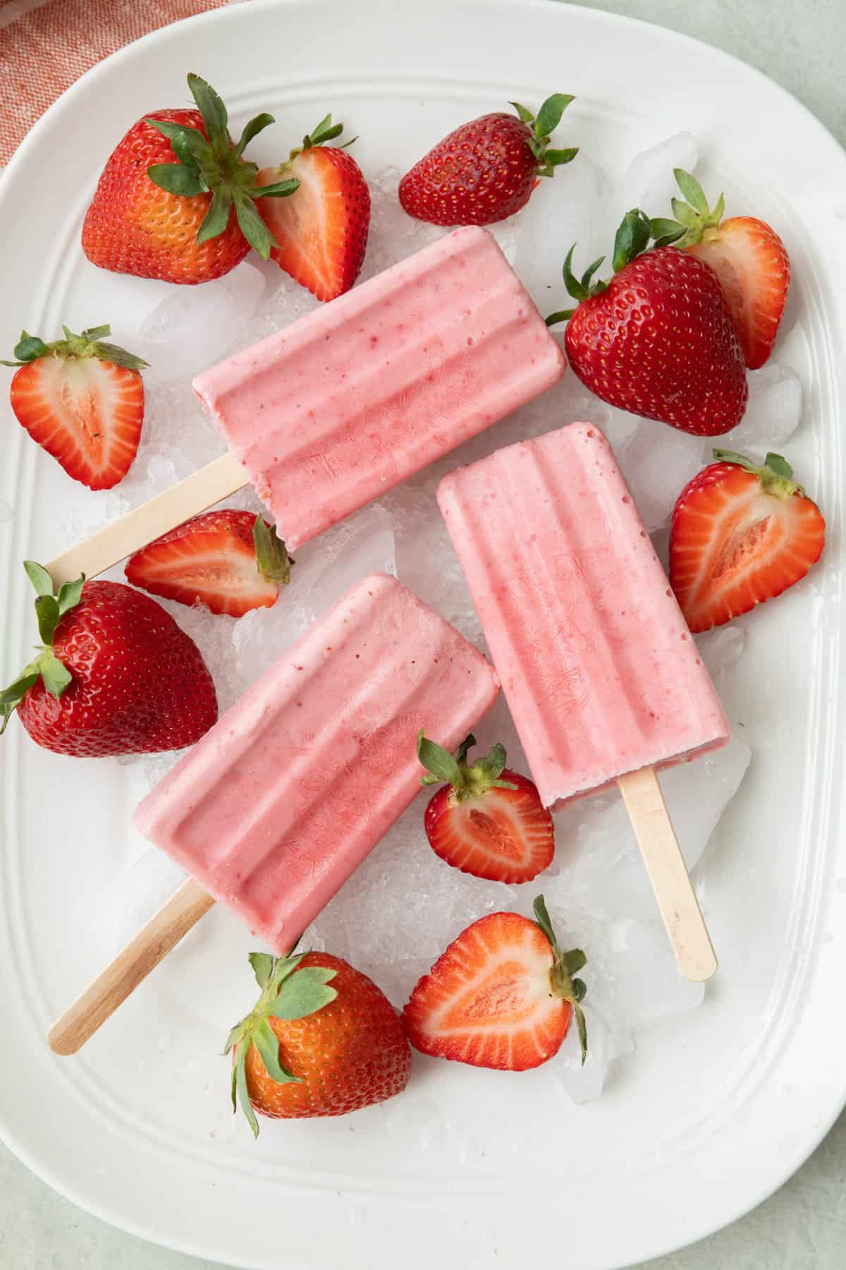 Frozen strawberry yogurt popsicles on a tray of ice with extra strawberries around.