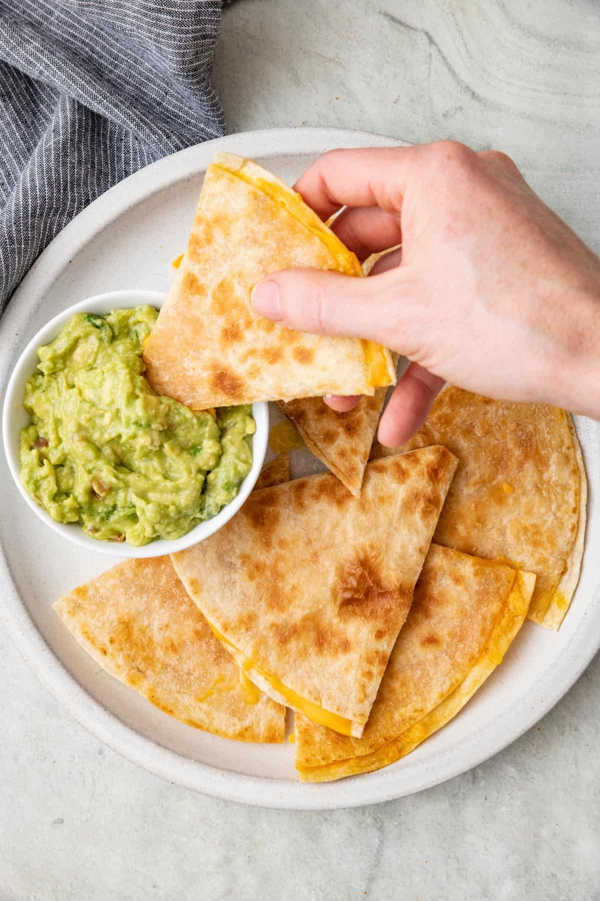 Cheese quesadilla slices on a plate with a side of guacamole with one piece being dipped into it.
