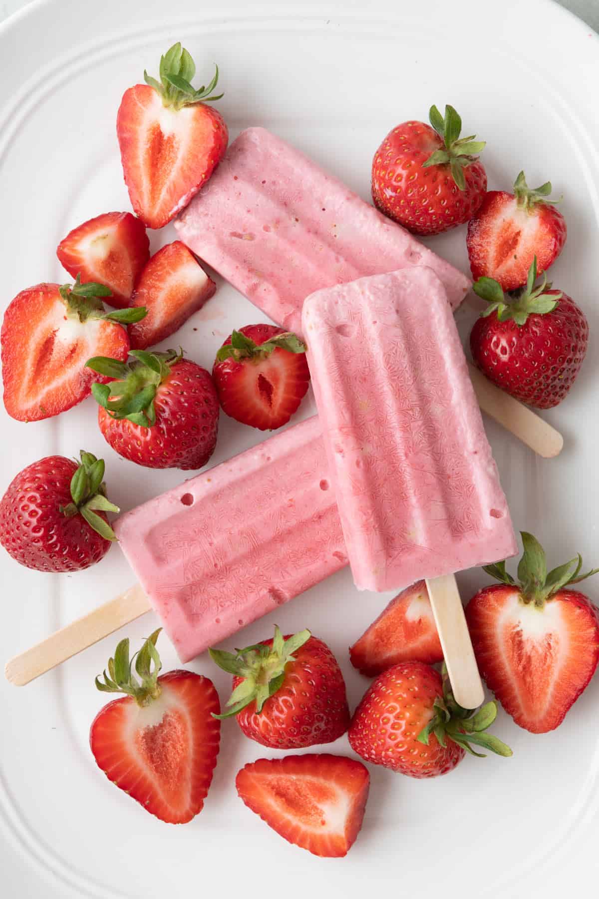 Frozen strawberry cheesecake bars on a tray with fresh whole and cut strawberries around.