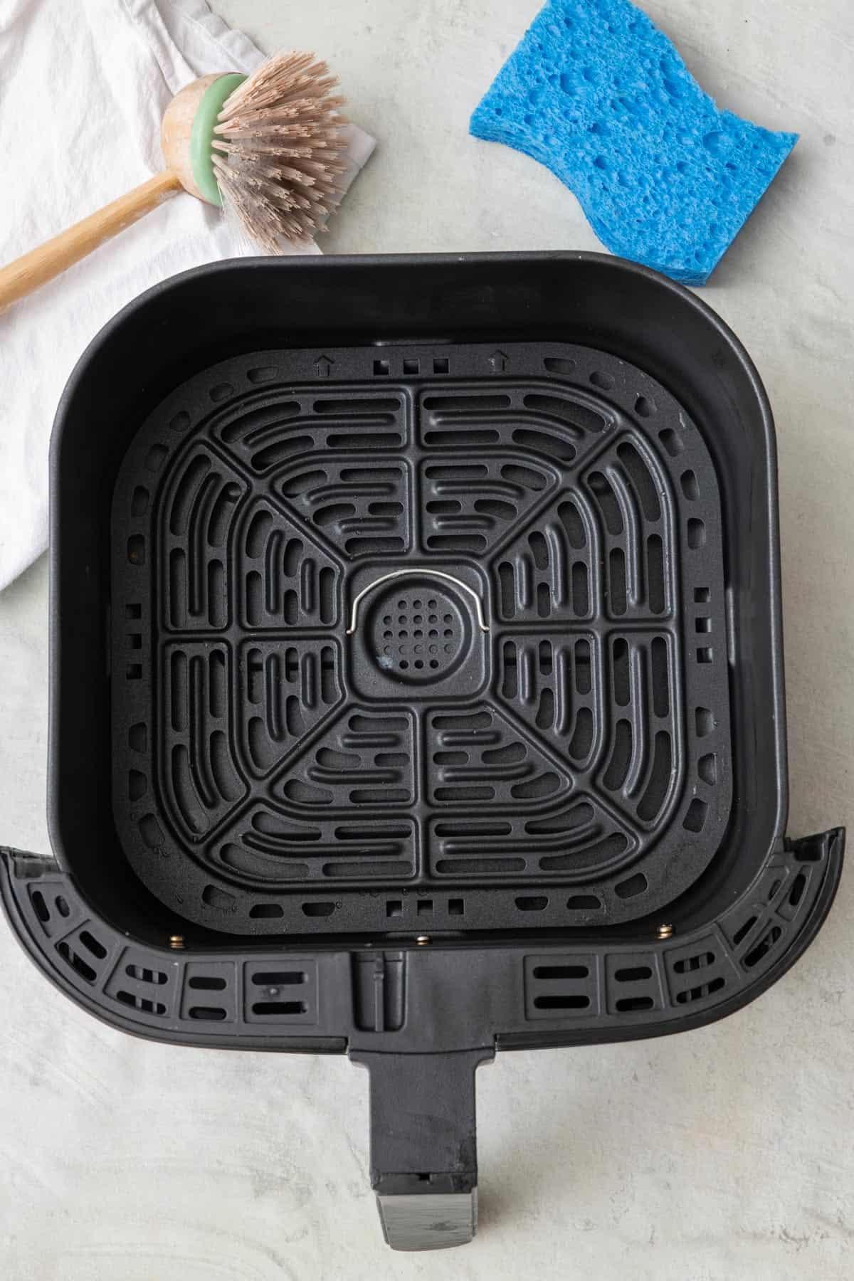 A cleaned up air fryer basket with a scrub brush and sponge nearby.