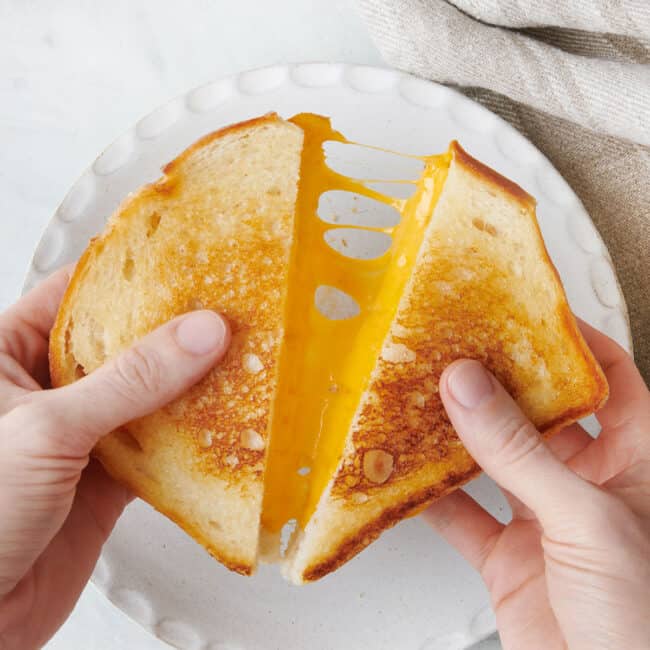 Grilled cheese cut in half and being pulled apart to show melty cheese.