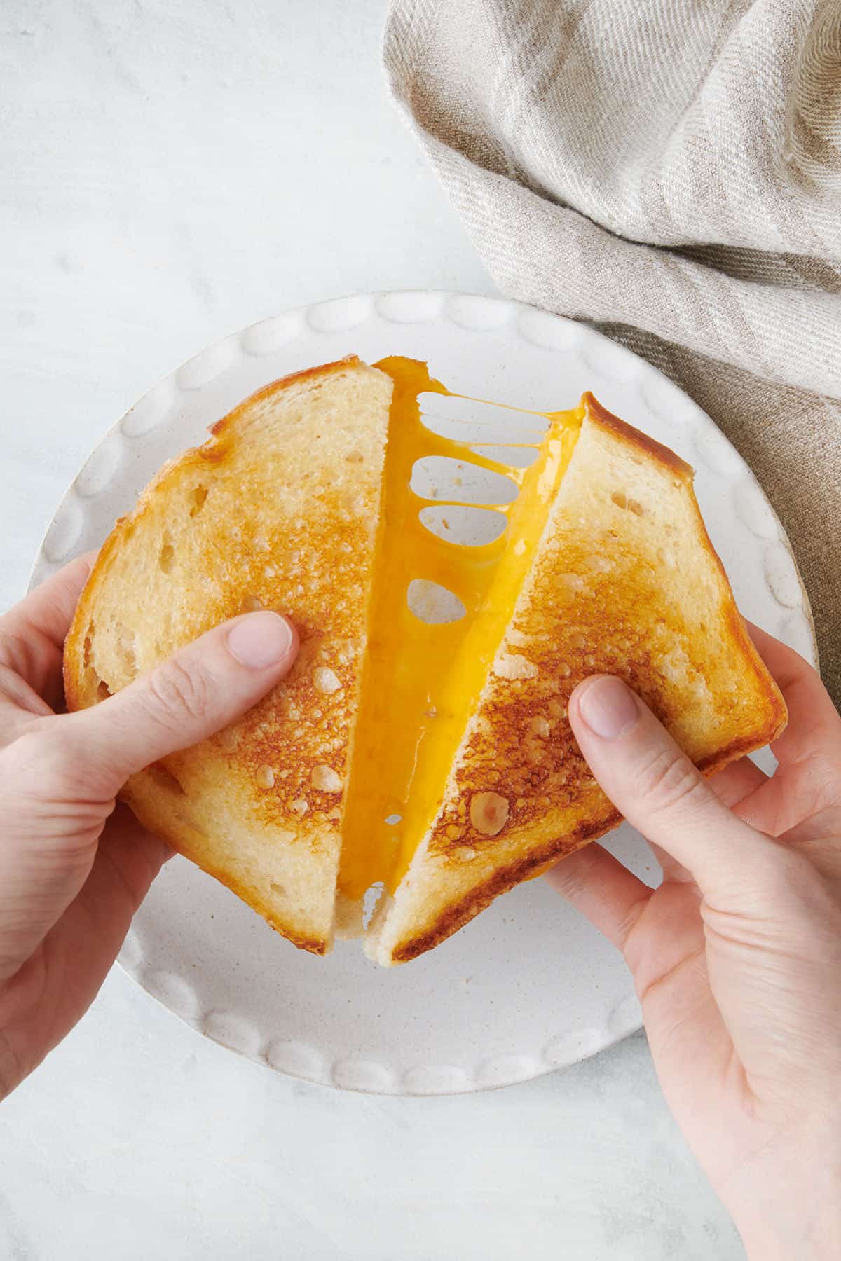 Grilled cheese cut in half and being pulled apart to show melty cheese.