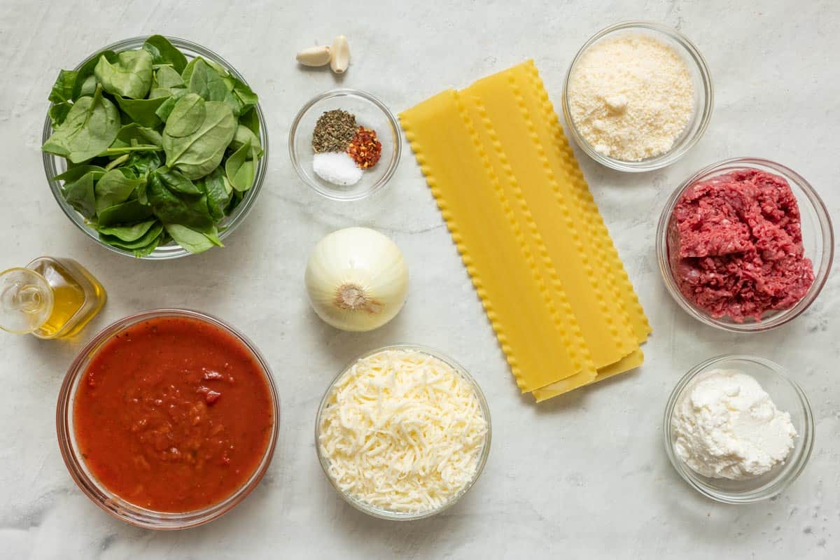 Ingredients for recipe: spinach, oil, marinara, shredded cheese, onion, spices, garlic, lasagna sheets, grated parmesan, ground beef, and ricotta.