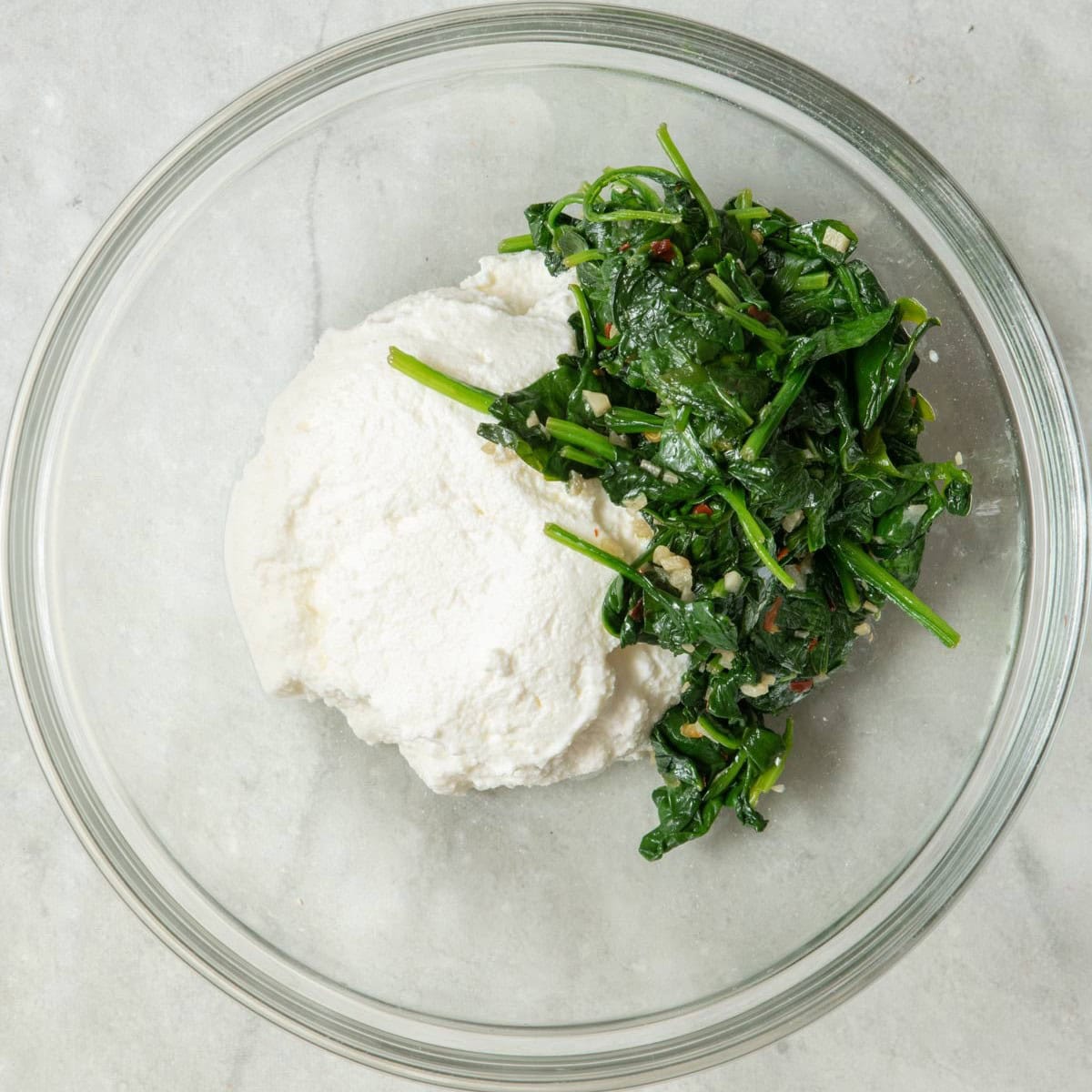 Spinach in a bowl with the ricotta added.