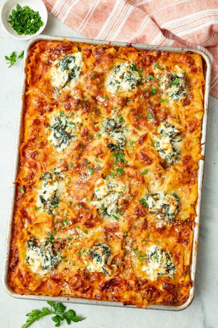Baked layerless lasagna on sheet pan garnished with fresh parsley and extra grated parmesan.