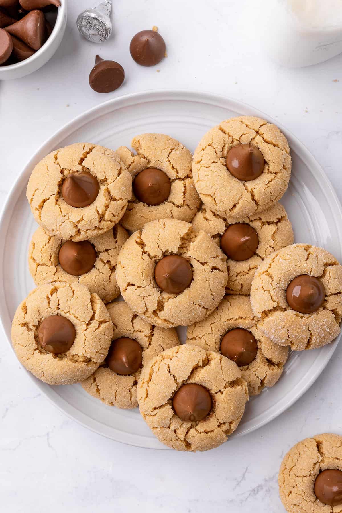 Peanut butter blossoms stack on a round plate with more Hershey kisses nearby.