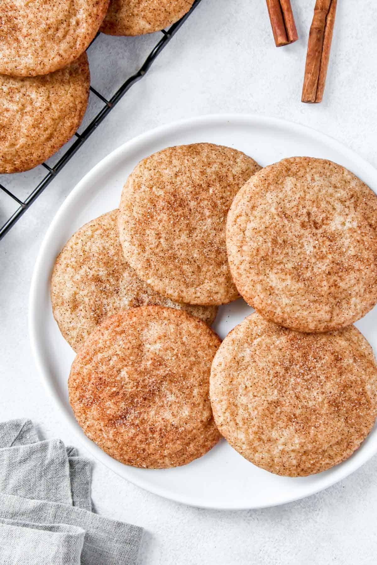 5 snickerdoodle cookies on a plate next to a wire rack with more on it.