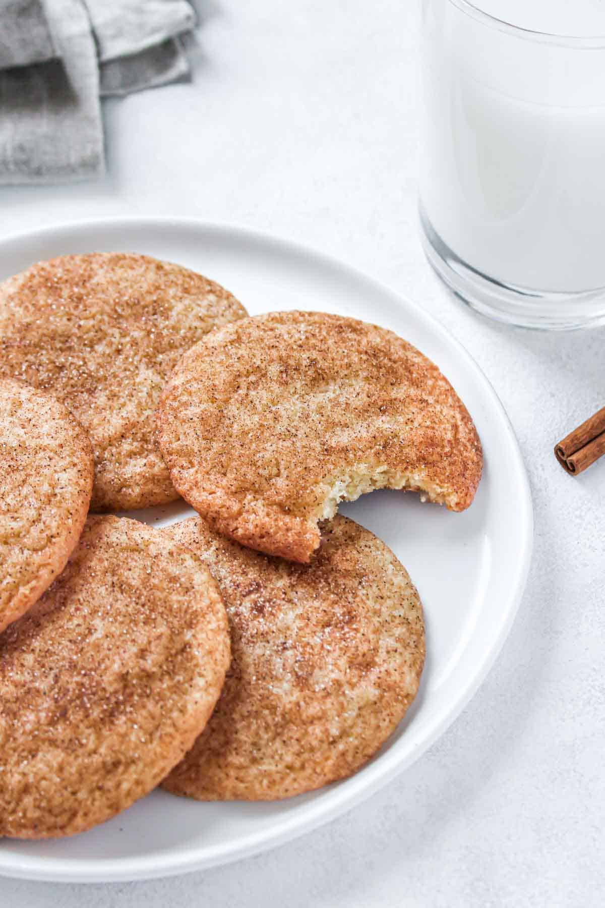 Snickerdoodles on a plate, one cookie with a bite taken out with a glass of milk nearby.