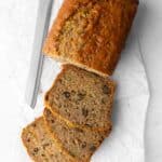 Zucchini bread on parchment paper cut halfway up into thick slices with a serrated knife nearby.