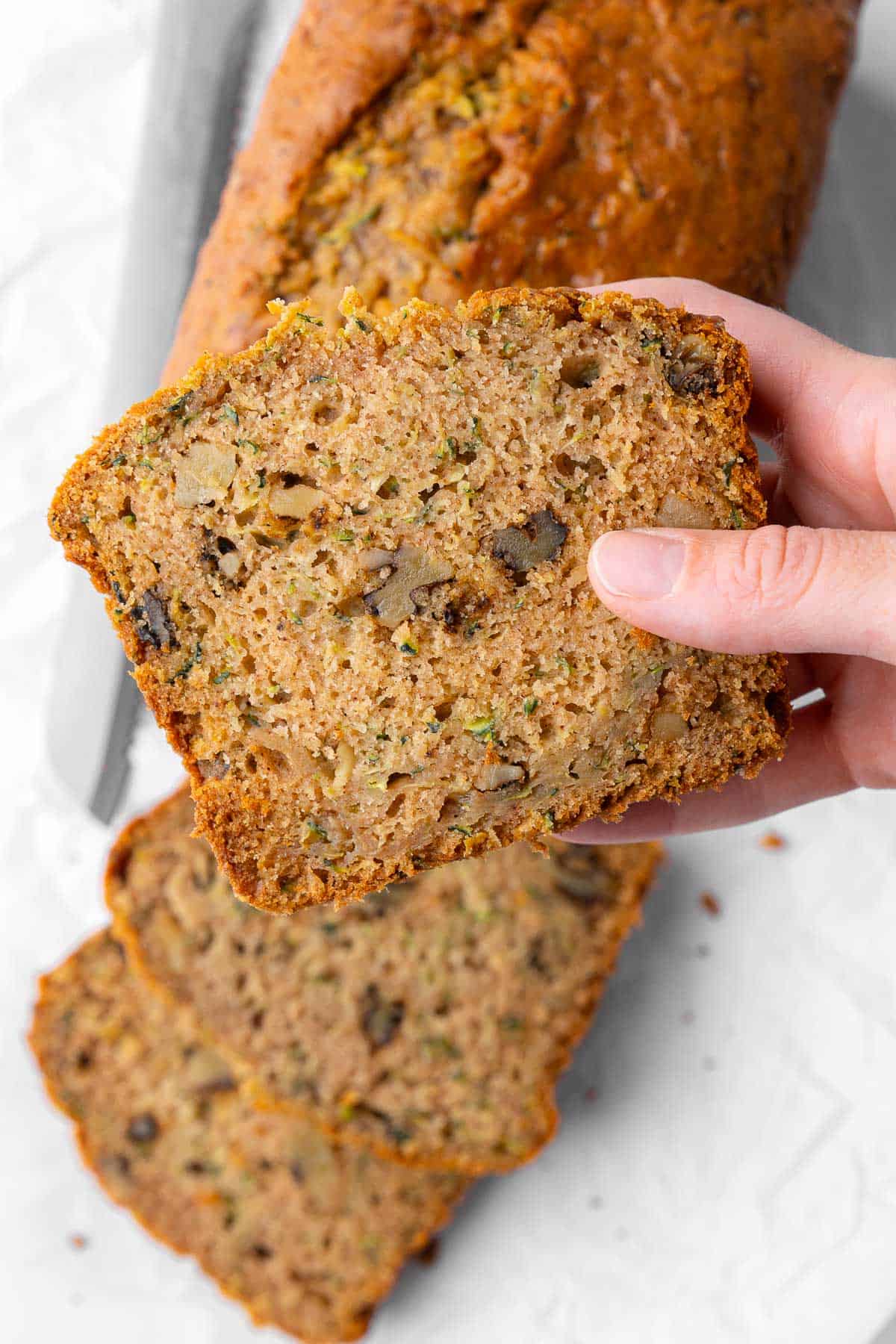 Hand holding a slice of zucchini bread up close to show texture.