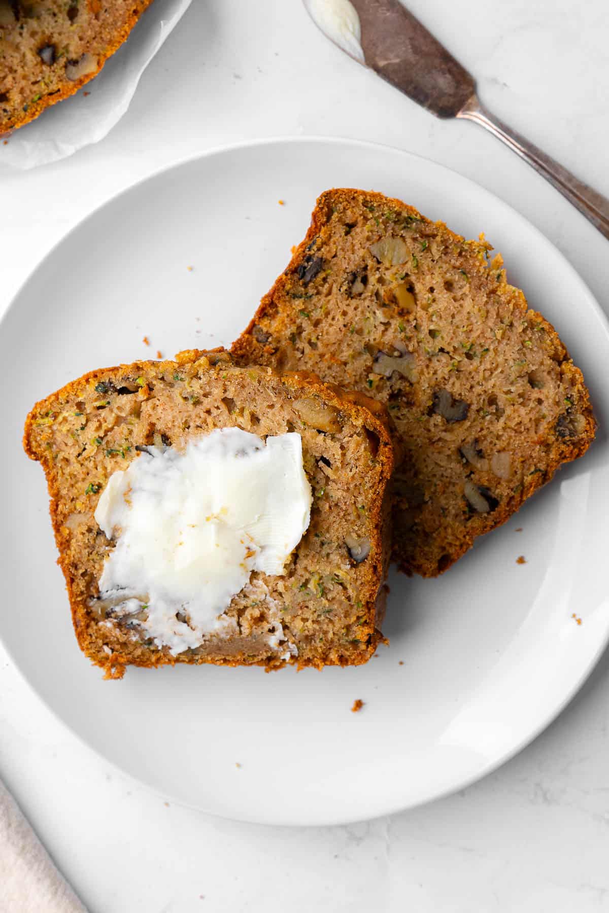 Zucchini bread slices on a plate, one smeared with butter.