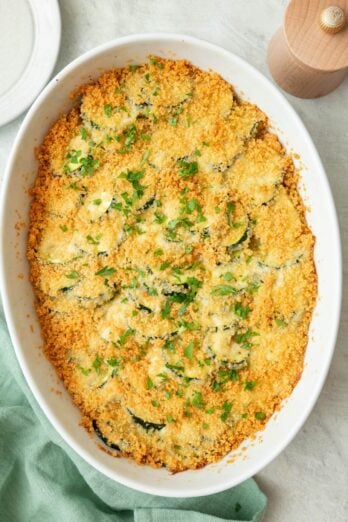 Zucchini casserole baked in an oval dish with a golden brown breadcrumb topping, garnished with fresh chopped parsley.