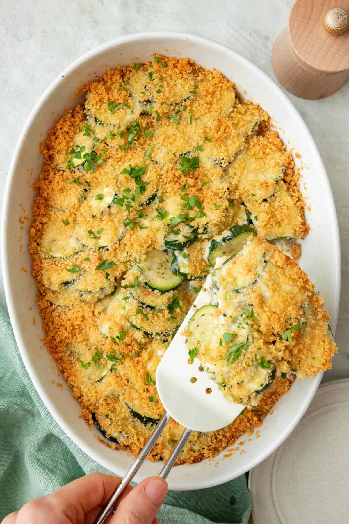 Zucchini casserole in a baking dish with a spatula lifting up a serving.