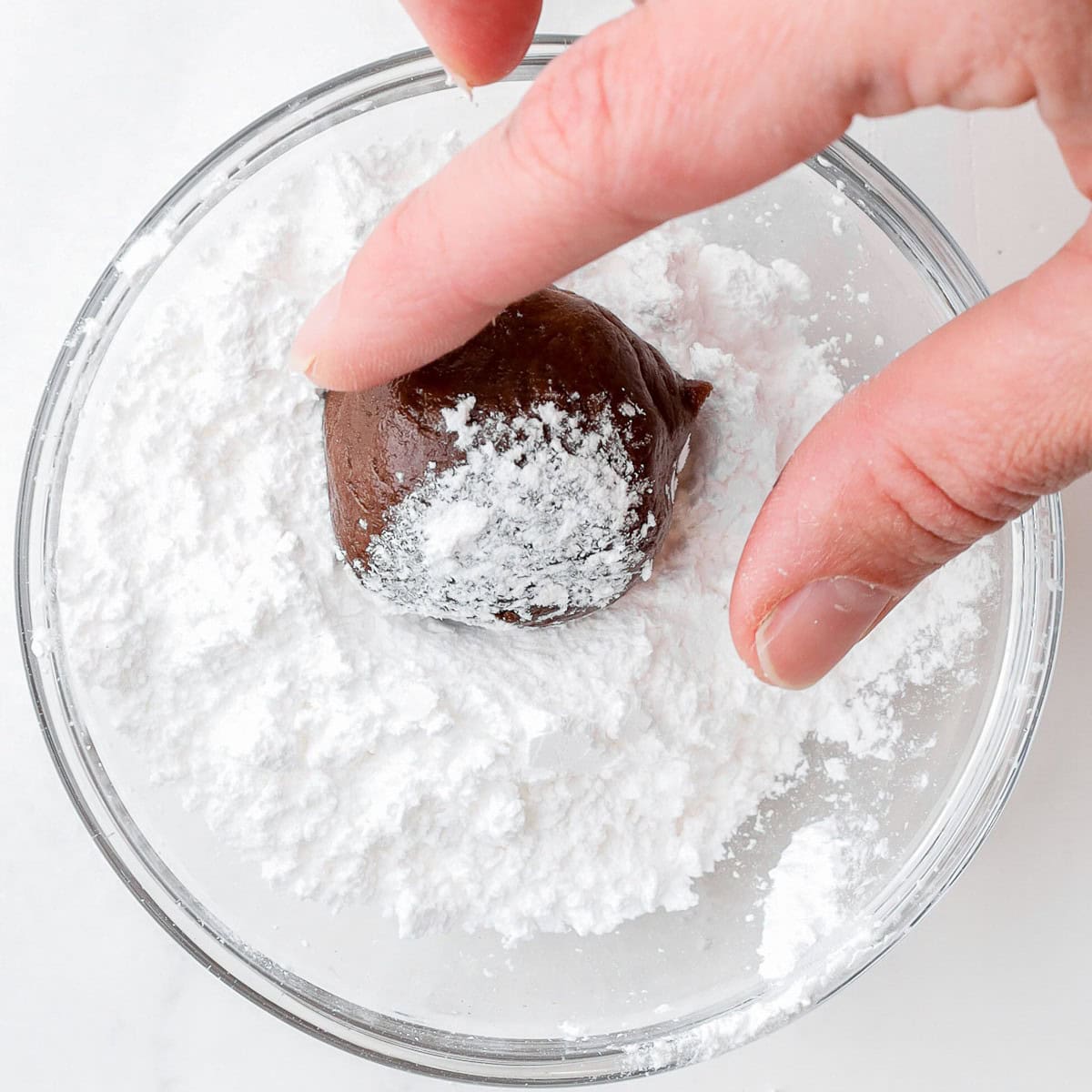 Rolling one cookie dough ball in the powdered sugar.