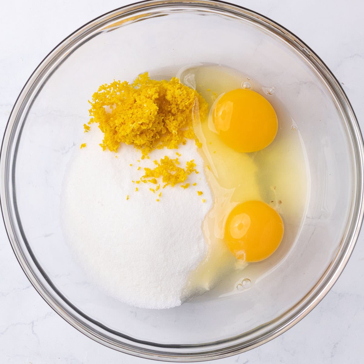 Sugar, orange zest, and 2 whole eggs in a bowl before mixing.