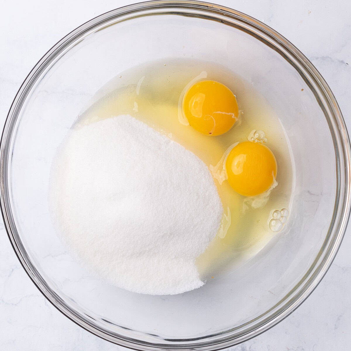 Sugar and 2 whole eggs in a bowl before mixing.