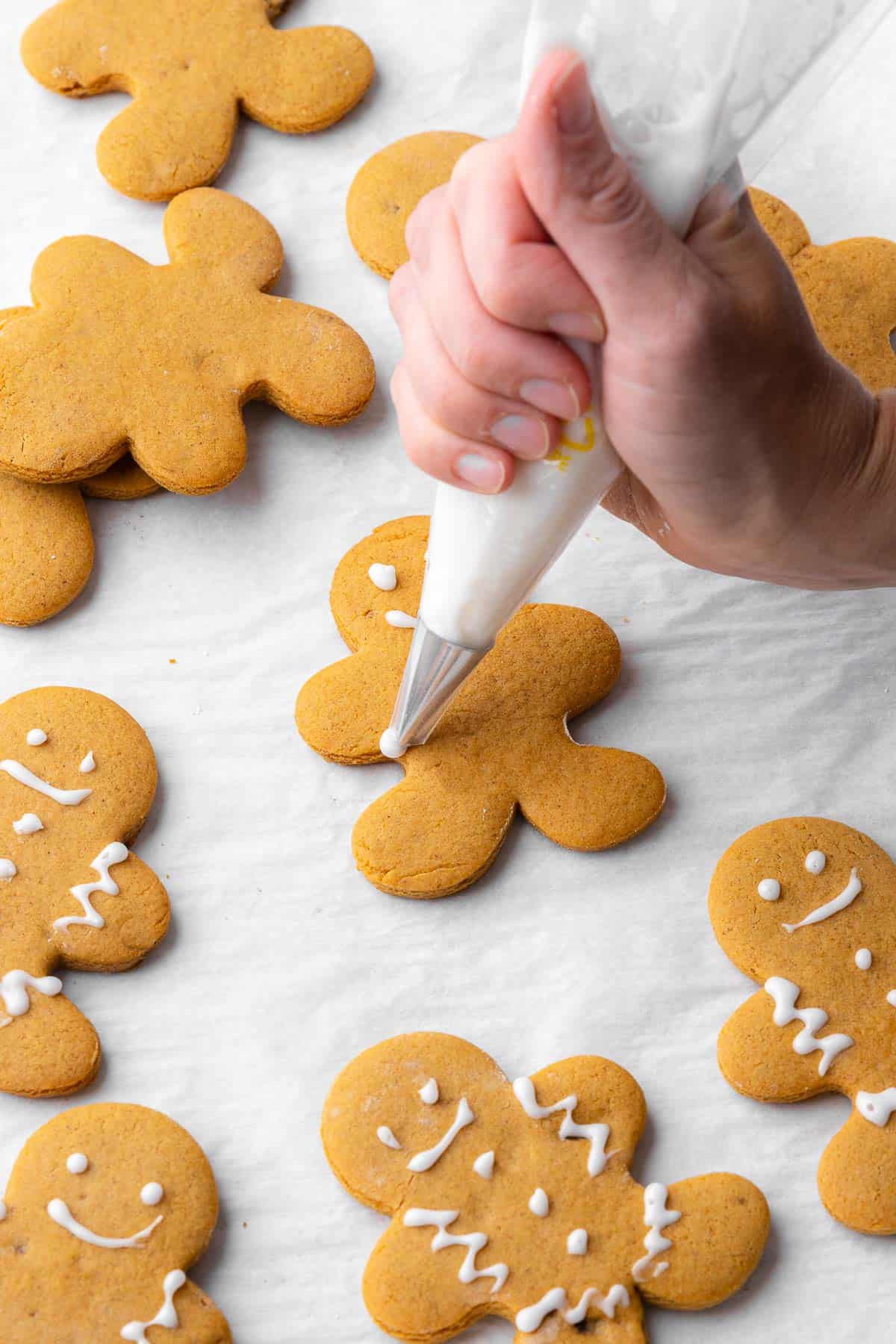 Piping icing decorations onto a gingerbread cookie with more cookies around.