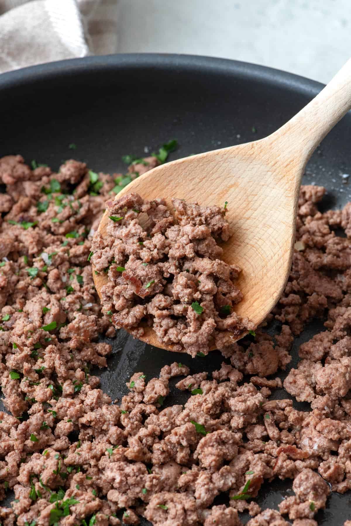 Round wood spatula lifting up ground beef from pan.