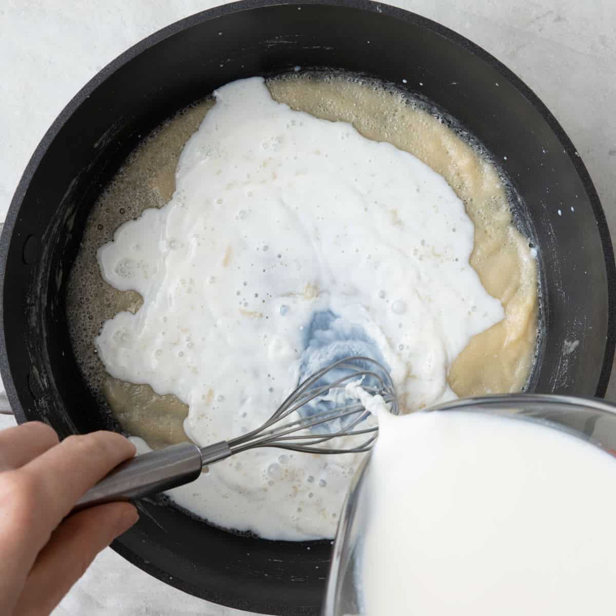Milk slowly being poured into pan while stirring.