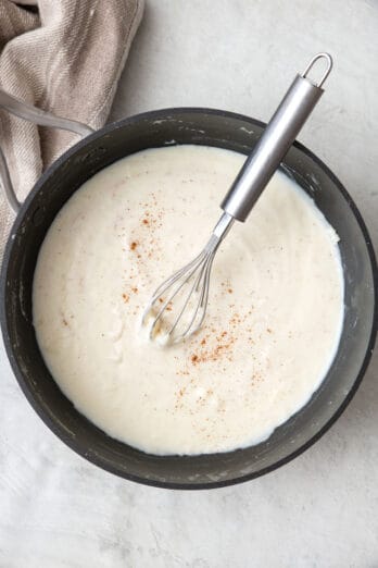 Bechamel sauce in a pot with a whisk dipped inside.