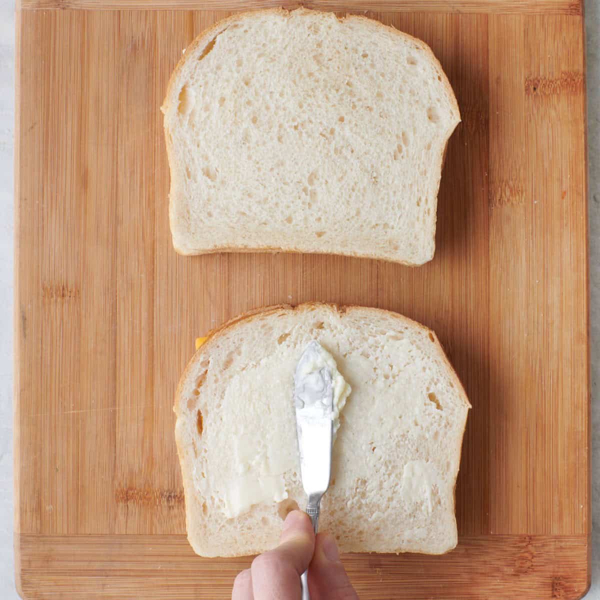 Buttering one side of the remaining two slices.