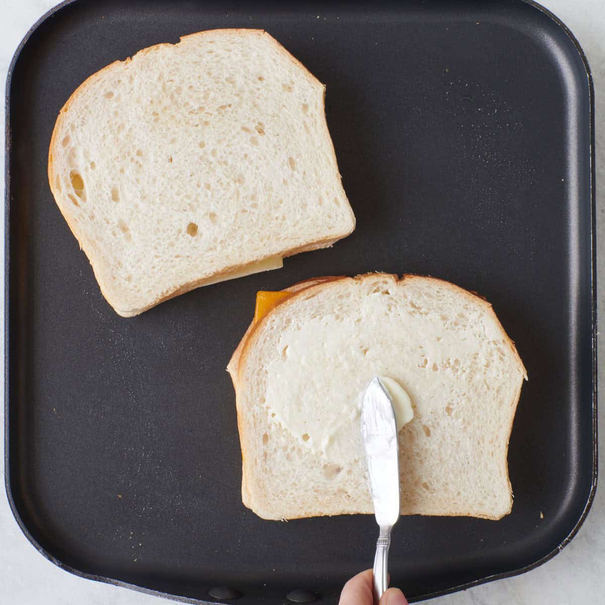 Sandwiches on pan, buttering the other side of the bread.