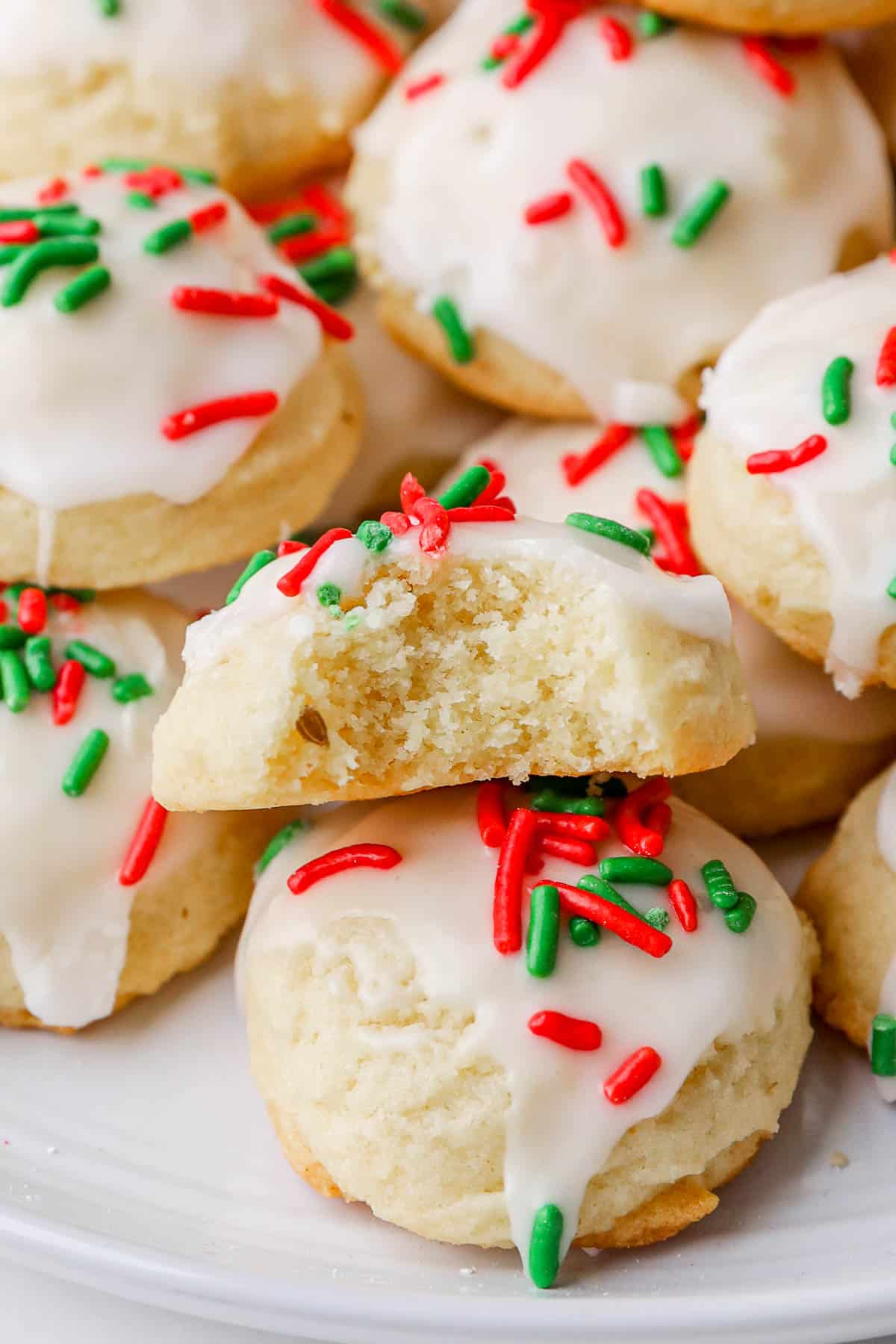 Close up of a plate of Italian Christmas cookies with a bite taken out of one to show texture.