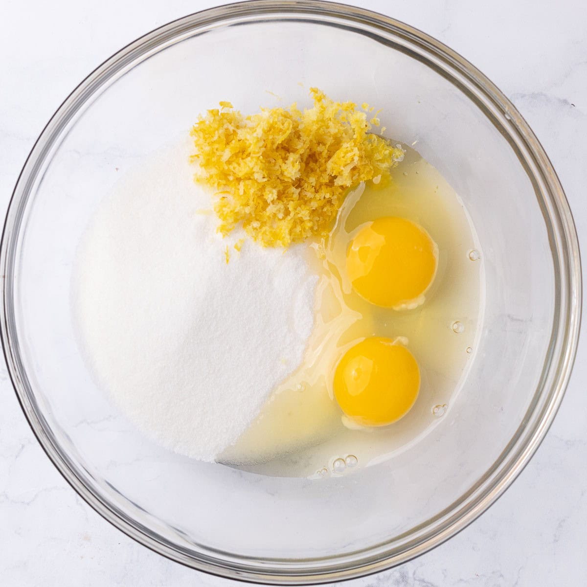 Sugar, zest, and 2 whole eggs in a bowl before mixing.