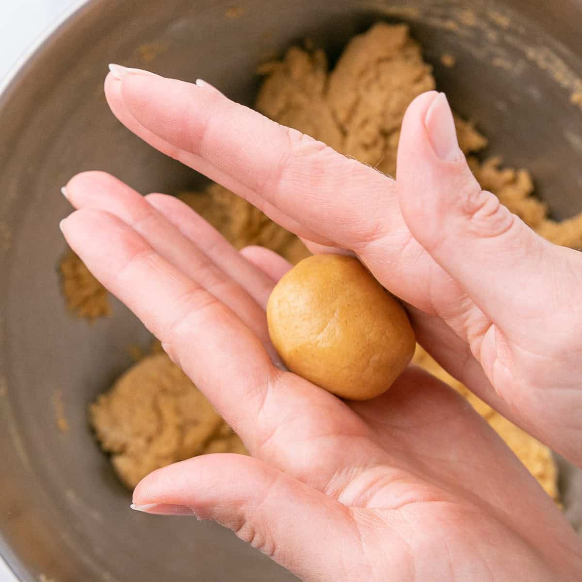 Hands rolling a dough ball in between palms into a smooth ball.