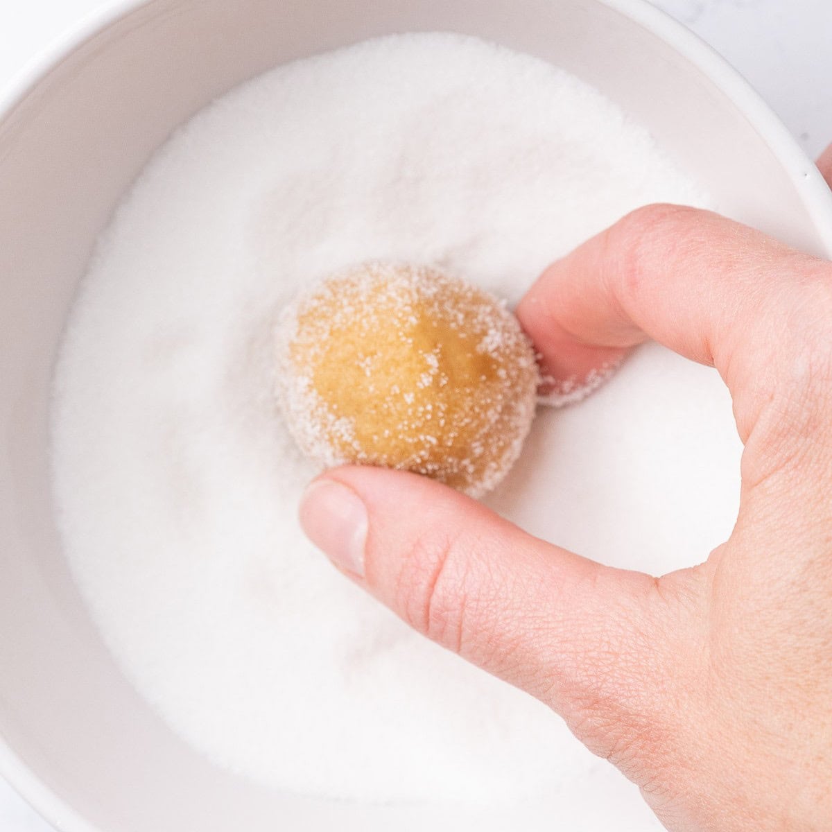 Hands coating a dough ball in sugar.