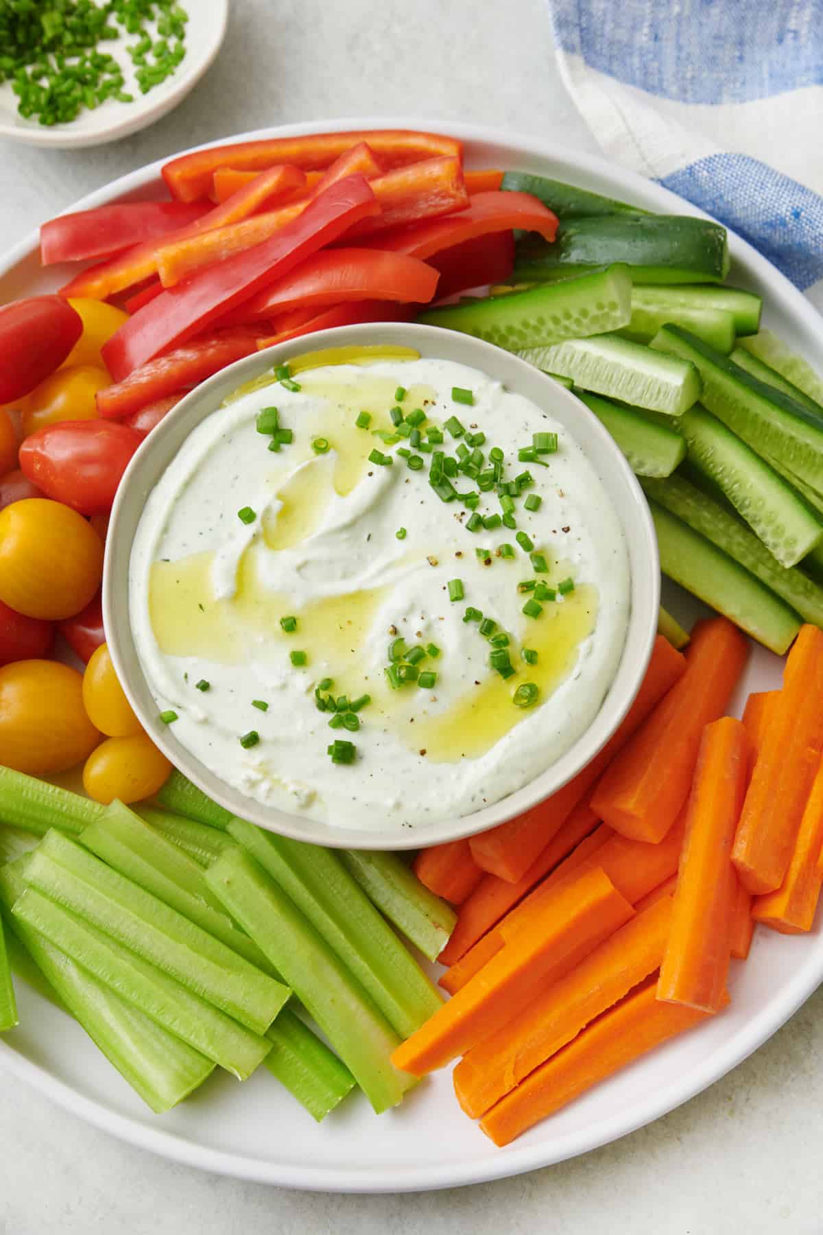 Close shot of a platter of fresh vegetables cut into sticks for dipping into a bowl of whipped cottage cheese garnished with chives and oil.