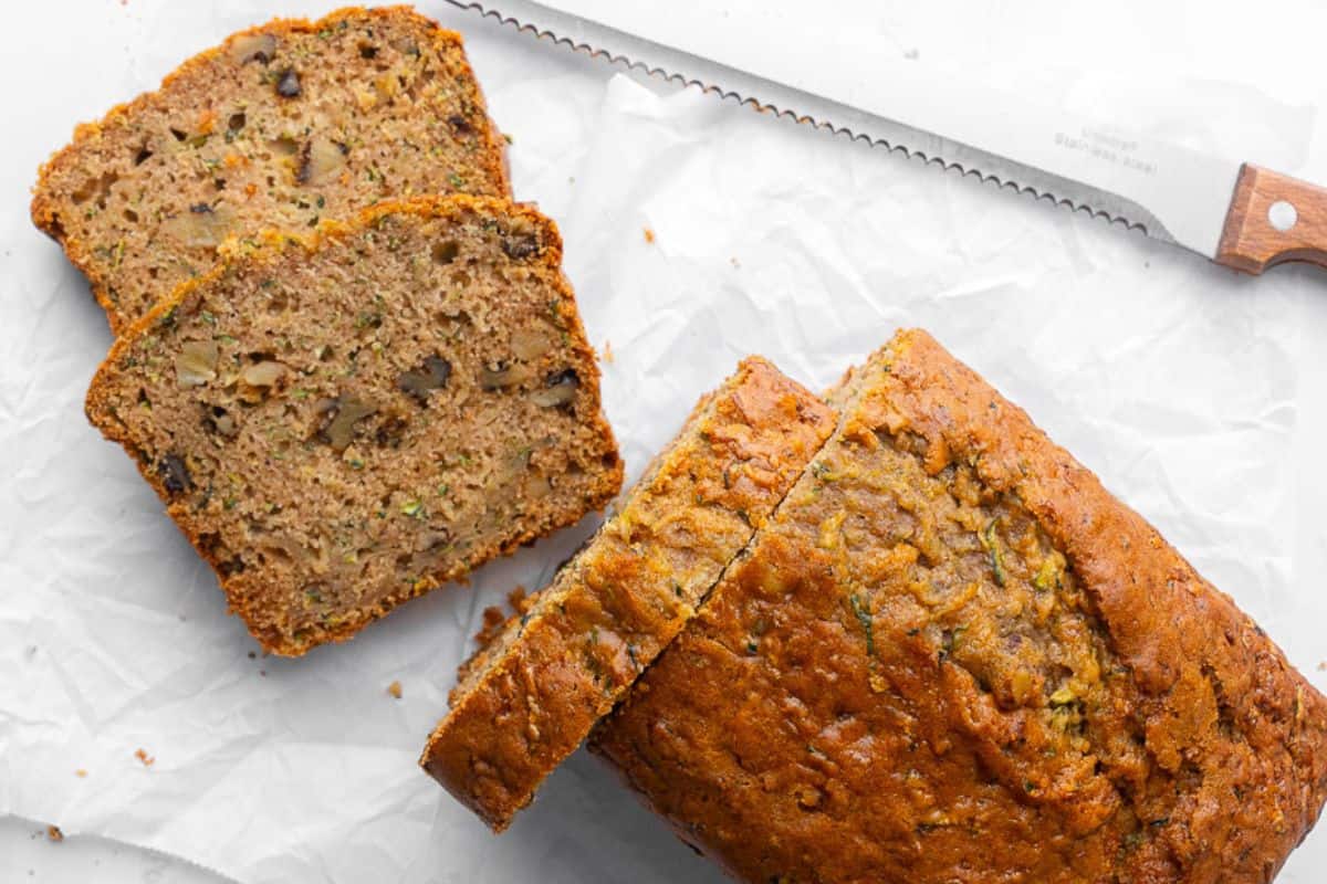 Zucchini bread sliced halfway with a few slices off to the side to show inside texture.