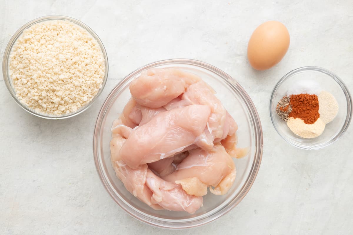 Ingredients for recipe in individual bowls: breadcrumbs, chicken tenders, an egg, and spice mix.