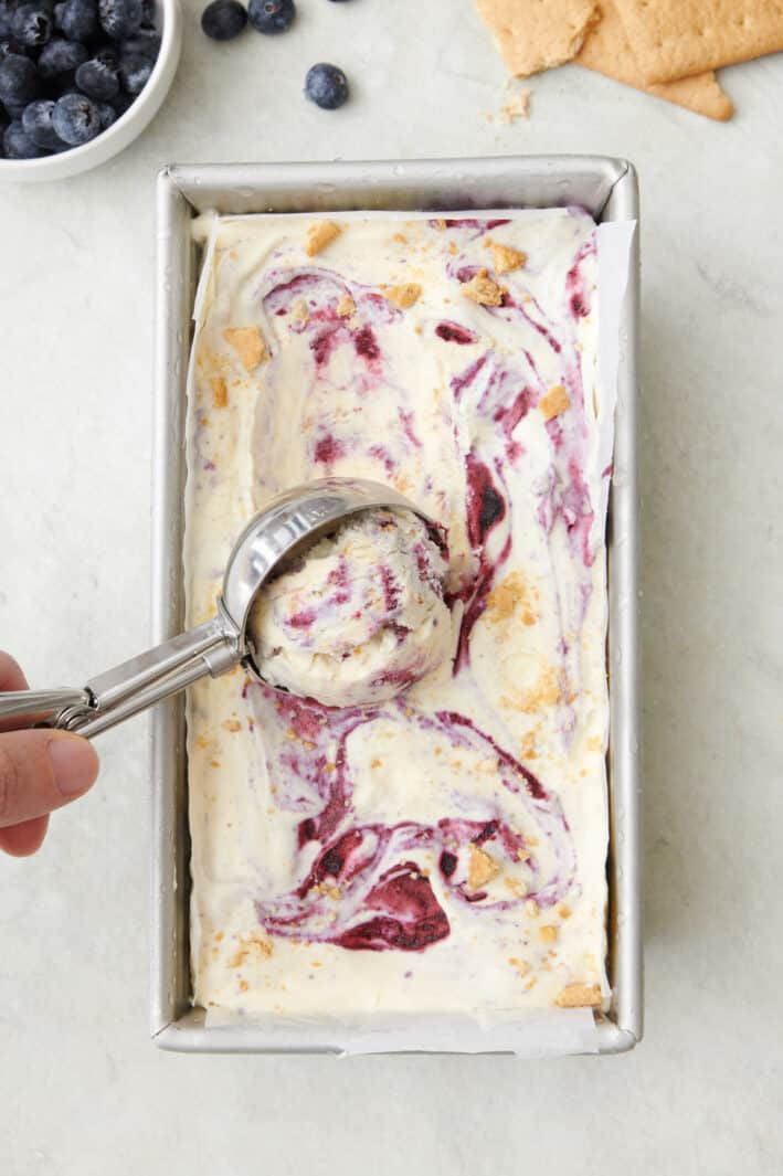Blueberry swirl ice cream being scooped out with an ice cream scoop after freezing.