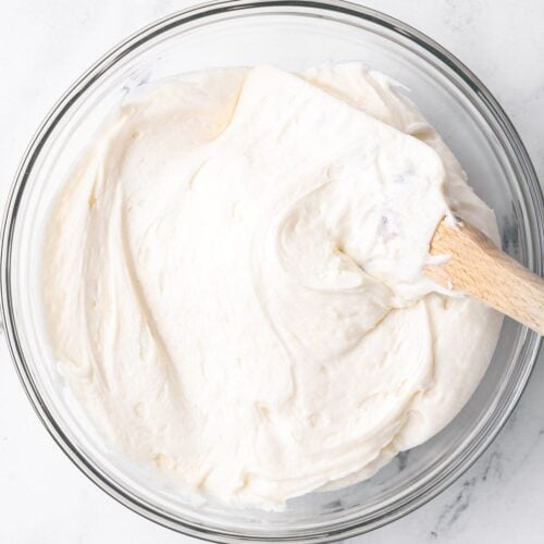 Square image of Buttercream frosting in a bowl with a rubber spatula dipped in.