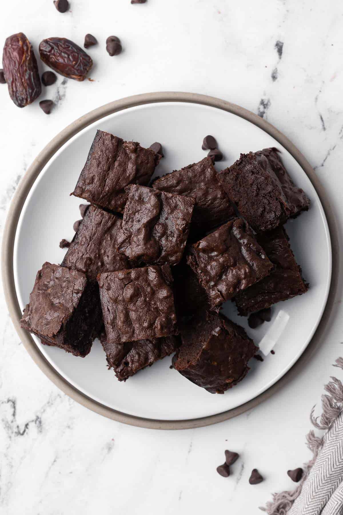 Date brownies squares on a round plate with a few chocolate chips and whole dates nearby.