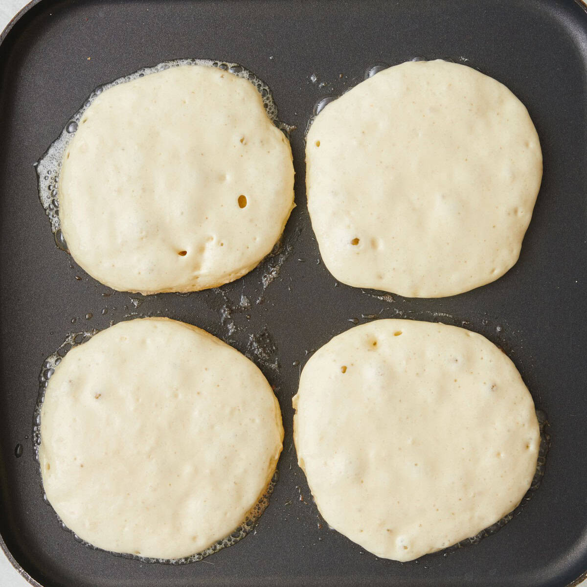 4 pancakes on a griddle before flipping.