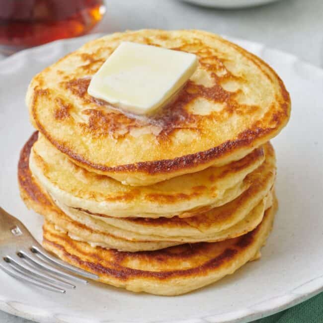 Stack of fluffy greek yogurt pancakes with a pat of butter on top.