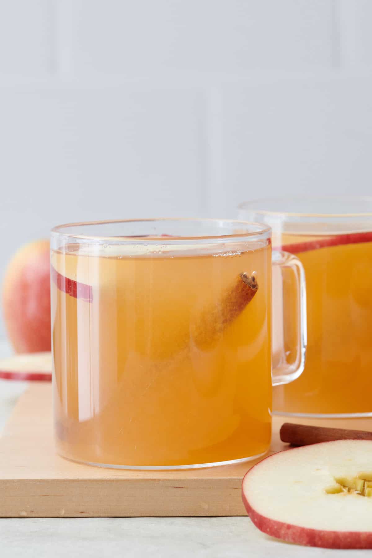 Homemade apple cider in a glass mug with a cinnamon stick and apple slice.